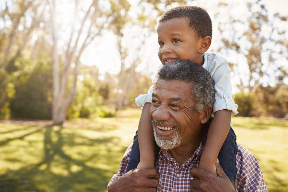 A grandfather carries his grandson on his shoulders during a walk in the park.