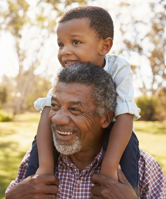 A grandfather carries his grandson on his shoulders during a walk in the park.