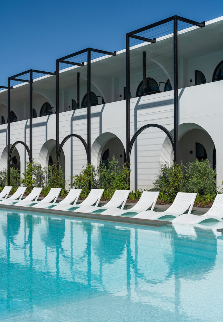 A view of the pool area at The Hazendal Hotel, featuring sun loungers and a striking wall with multiple arched openings in the background.