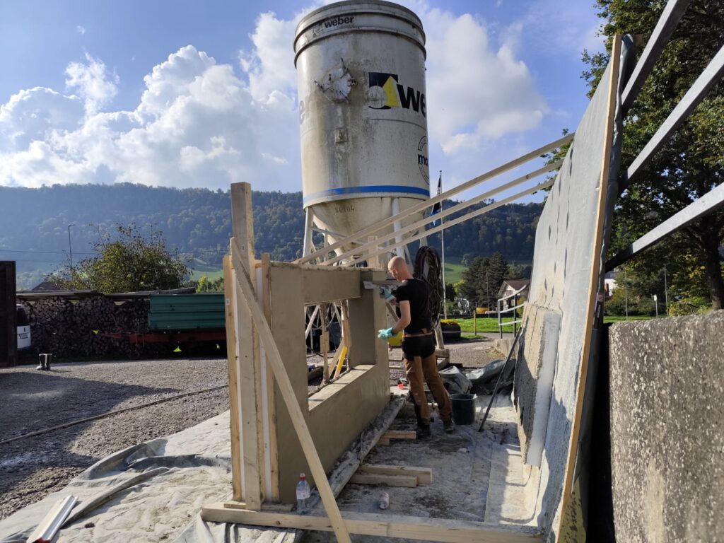 Back view of a Citra Building Technology wall mock-up, showing a construction worker smoothing the rear plaster surface.