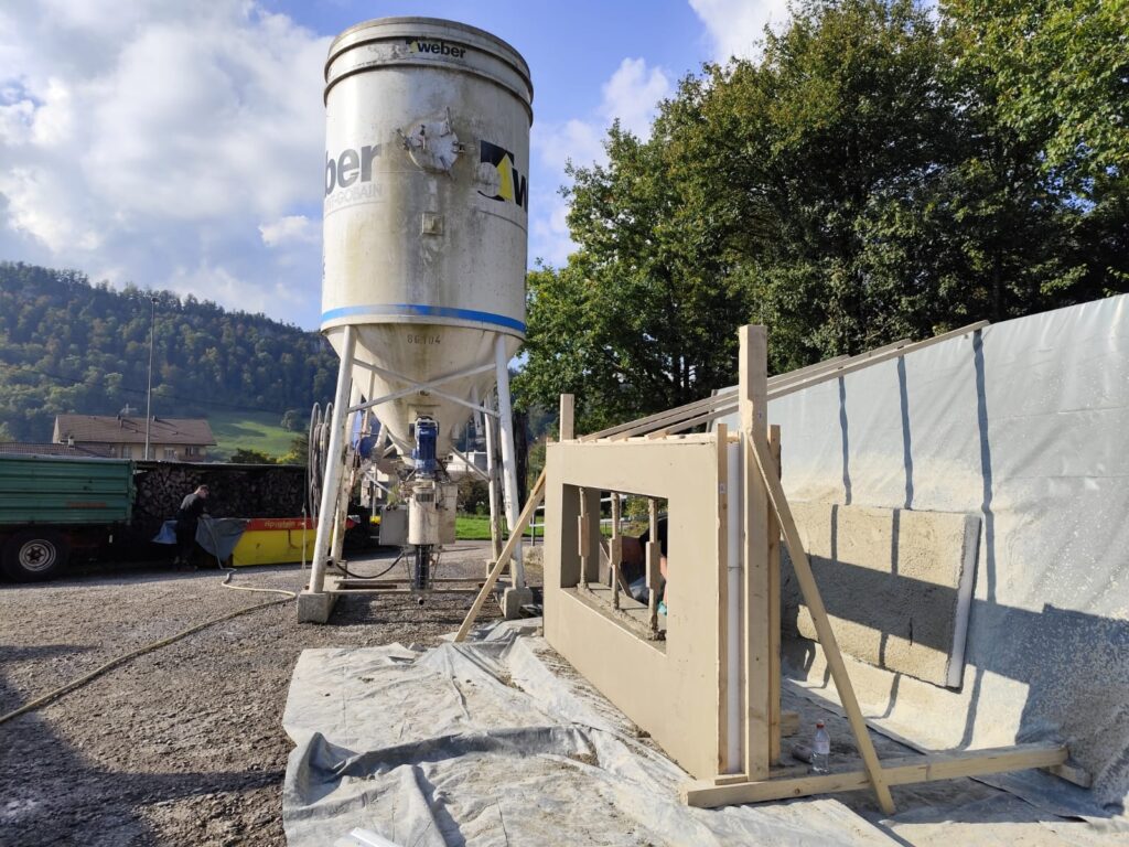 A worker smoothing the plaster of a Citra Building Technology wall mock-up, seen from a side angle that specifically shows the wall's structural thickness.