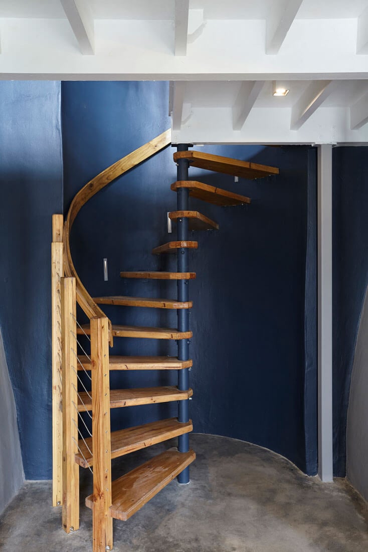 Wooden spiral staircase with dark blue wall background, modern interior design, and concrete floor.