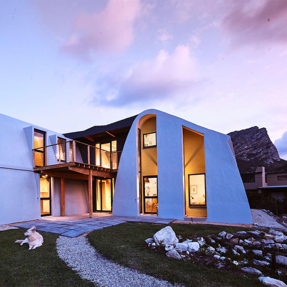 Modern architectural house with curved design and large windows at sunset.