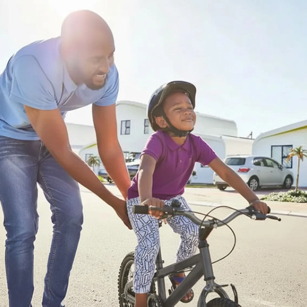 Father assisting young girl on a bicycle in a bright outdoor setting.