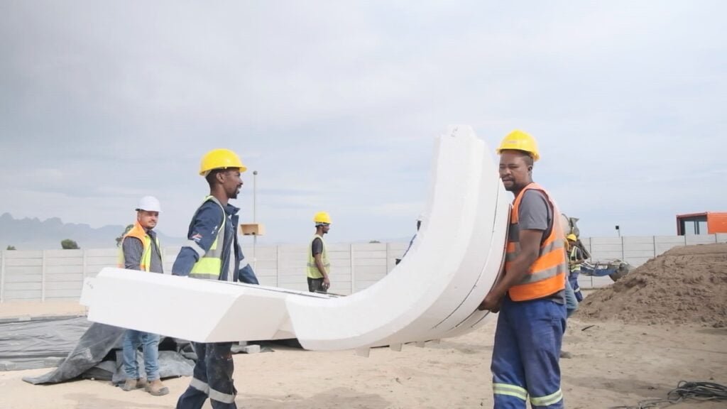 Construction workers installing large white curved concrete structure at site.