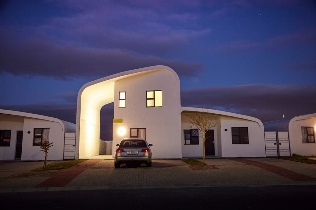 Modern white residential building with unique curved design and illuminated windows at dusk, showcas.