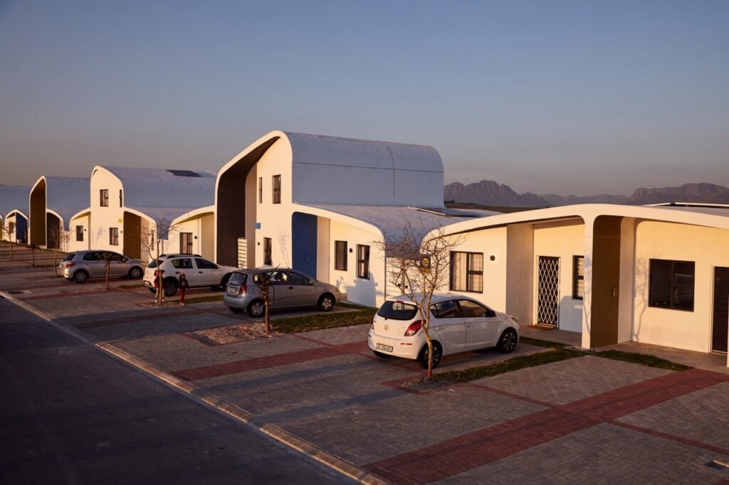 Modern residential housing development with unique curved architecture and parked cars in a suburban.