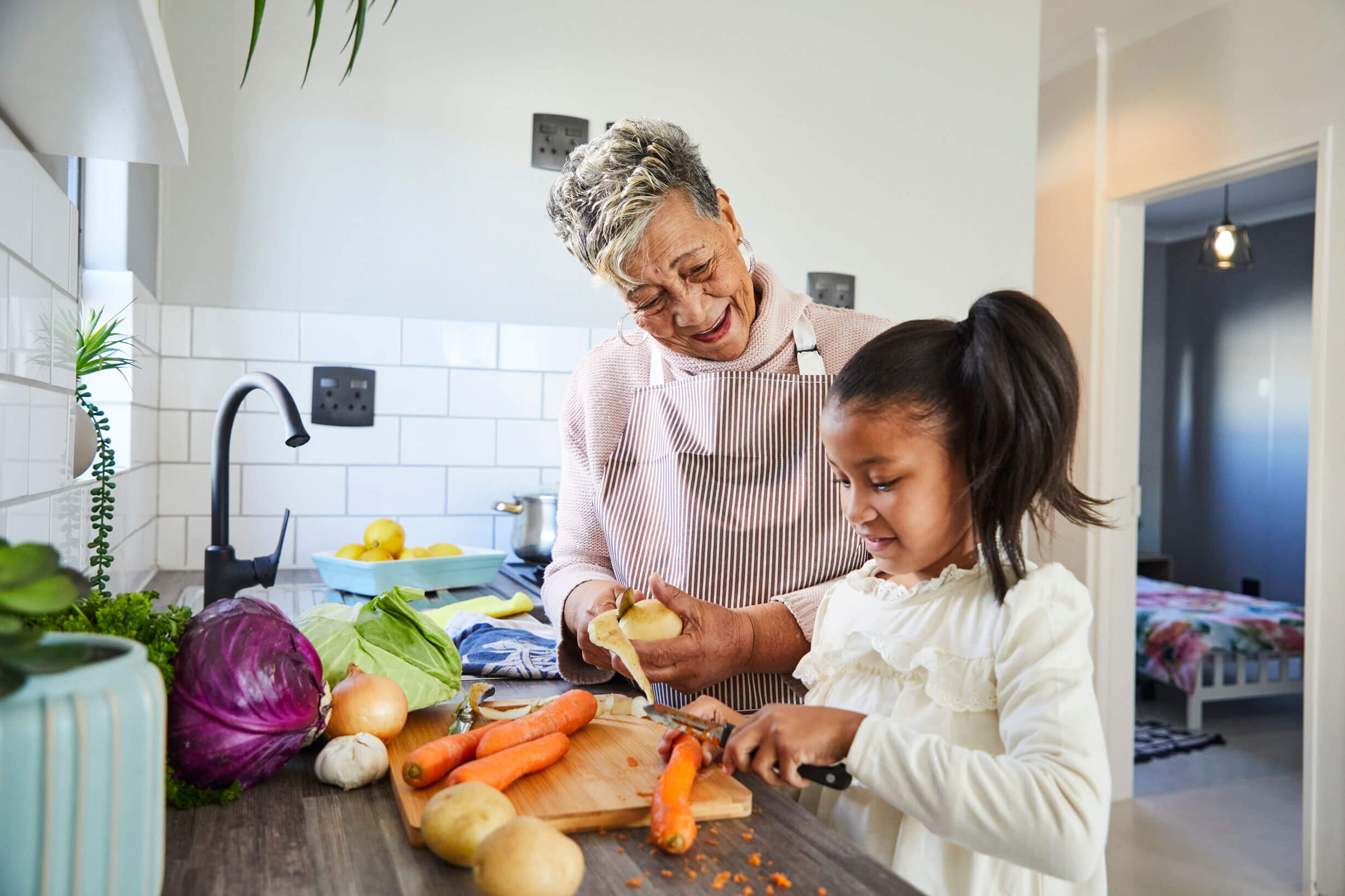 Fresh vegetables and a joyful grandmother and granddaughter preparing a healthy meal in a modern kit.
