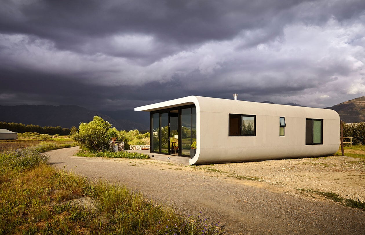 Modern minimalist tiny house with curved design and large glass windows in a rural setting.