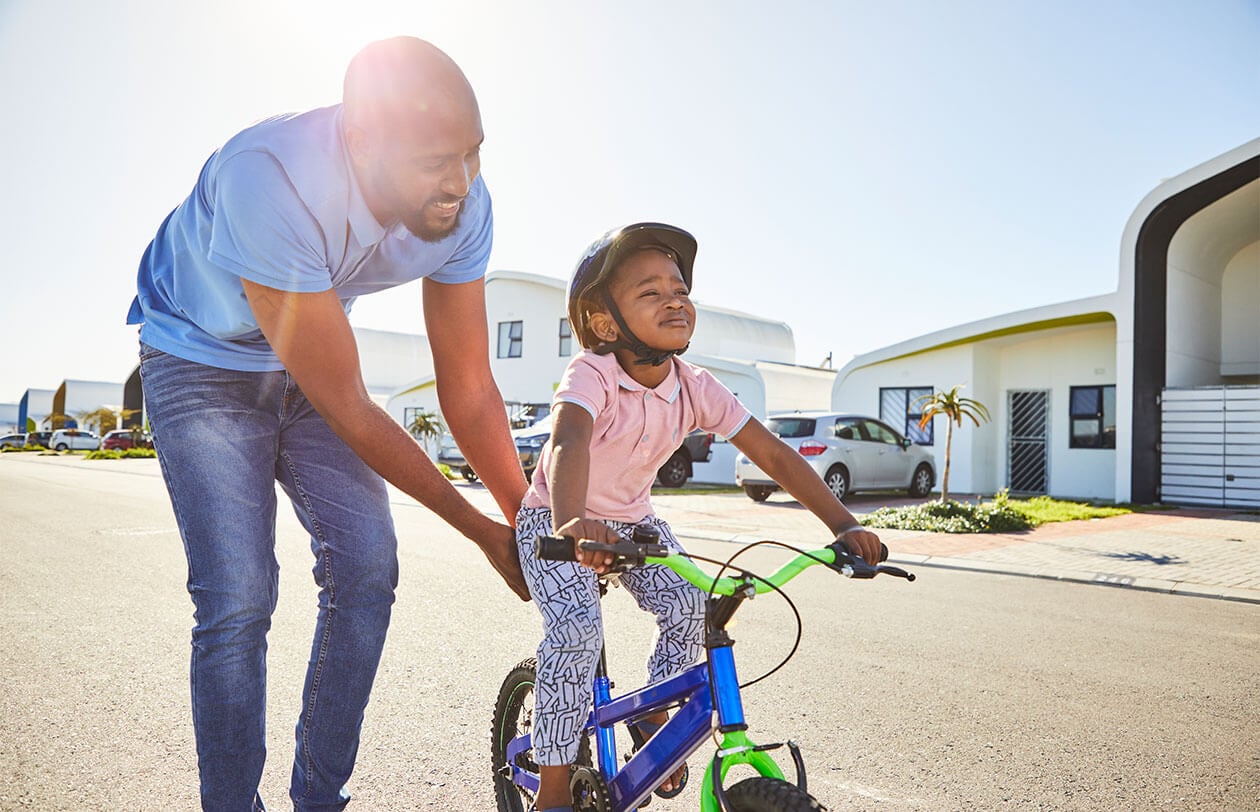 Father helping daughter learn to ride a bike outdoors.