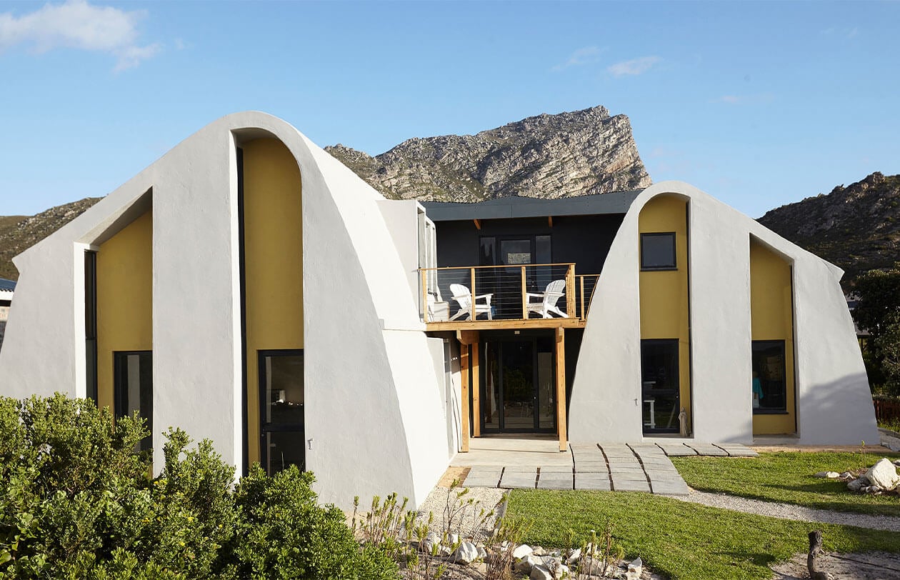 Unique modern mountain house with curved white walls and large windows in a scenic landscape.