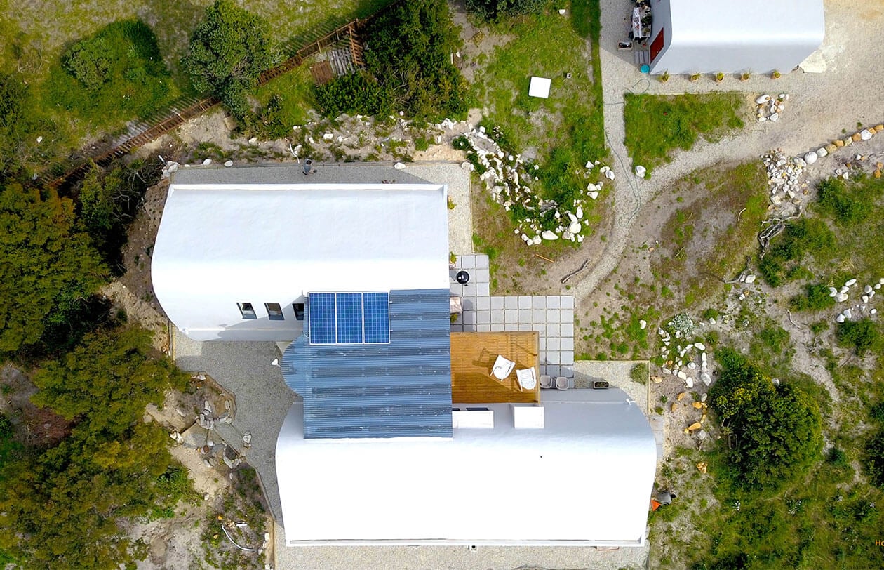 Eco-friendly house with solar panels, white roof, and surrounding greenery in South Africa.